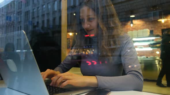 Beautiful Caucasian Girl Freelancer Working in a Cafe at the Computer and Drinking Coffee, .