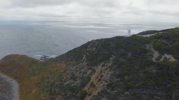 Aerial of a lonely lighthouse on top of a high cliff overlooking a big ocean on a dark stormy day.