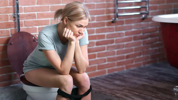 Bored Pensive Young Woman Sitting on Toilet at Home Bathroom Medium Long Shot