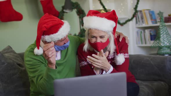 Happy senior caucasian couple celebrating christmas wearing face maska and santa hats