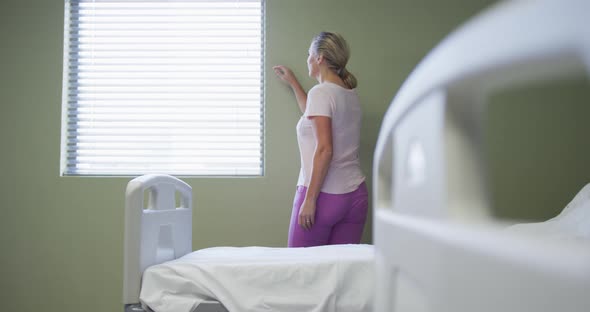 Caucasian female patient standing in hospital room looking at window