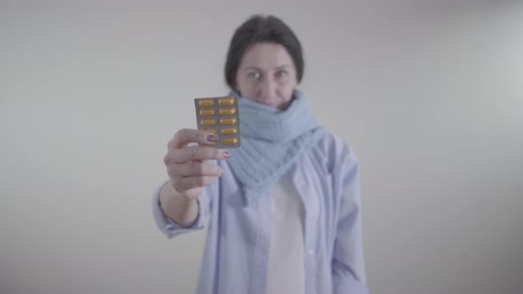 Close-up of Female Caucasian Hand Holding Blister Pack of Pills. Blurred Adult Woman in Warm Scarf