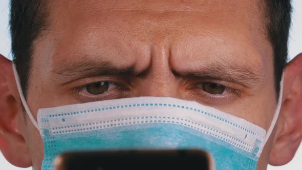 Man in Protective Face Mask Looks at Smartphone Holding It in Hands on Street