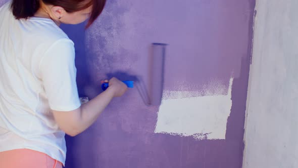 Close Up of Young Woman Painting Wall in Purple Colour with Roller