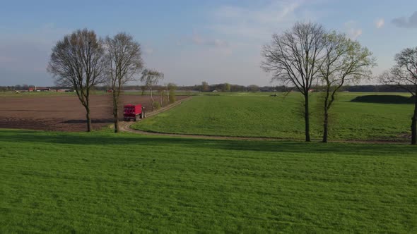 AERIAL Drone Shot Modern Tractor Hauls an Empty Trailer Down a Dirt Road Crossing the Farmfields