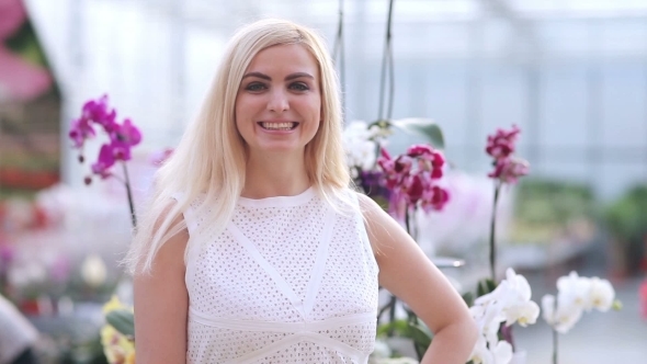 Woman Smiling To Camera With Orchid On Background alt