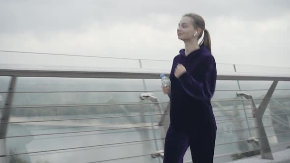 Confident Smiling Sportswoman Running with Water Outdoors