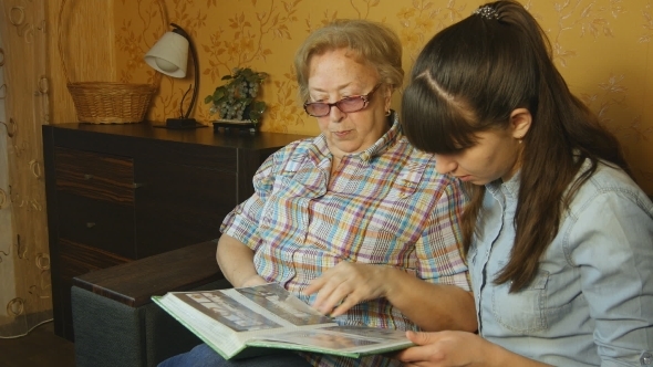 Old and Young Woman Looking at Family Photo Album on Sofa at Home