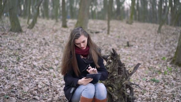 Beautiful Girl Sitting On a Stump And Using Tablet. 