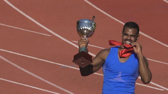 Happy Athlete Biting His Medal Showing It Is Gold, Winner Celebrating Triumph