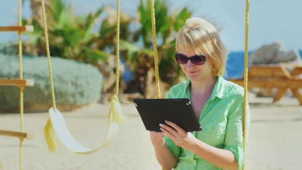 A Female Tourist Enjoys The Tablet, Sitting On a Swing