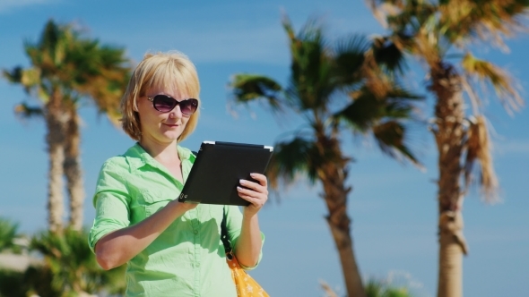 A Woman In a Light Green Shirt Using Tablet Against The Sky And Palm Trees