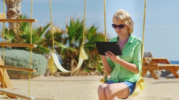 Woman Sitting On a Swing And Enjoys Tablet