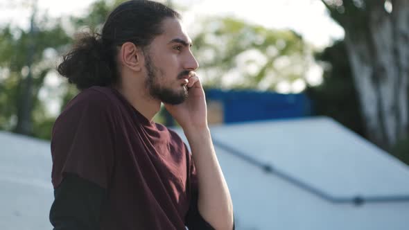 Portrait of Young Attractive Arab Man Sitting on the Grass and Talking on the Phone