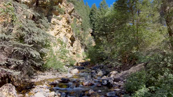 Mountain Valley Stream below rugged cliffs - aerial pull back in slow motion