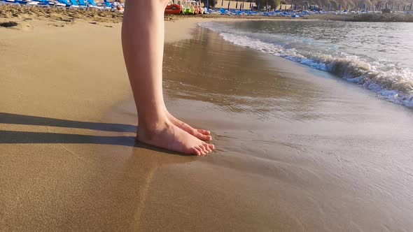 A woman wiggles her toes in the sand while standing in the waves at the beach