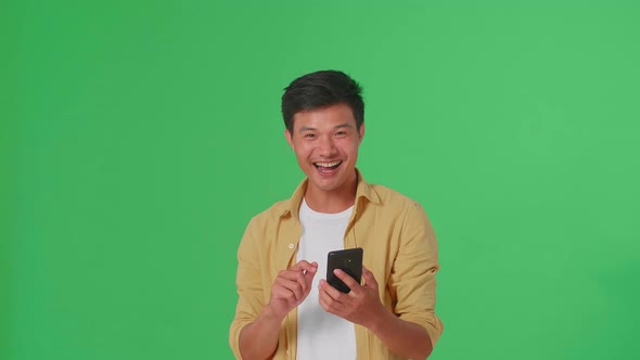 Young Asian Man Surprise And Say Wow During Use Mobile Phone In Green Screen Studio