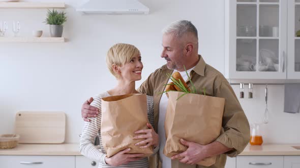 Happy Family Couple Posing Holding Grocery Shopping Bags In Kitchen