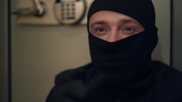 Portrait of Young Caucasian Thief in Black Clothes and Balaclava Rubbing His Hands. The Guy Stealing