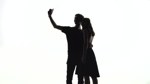 Silhouettes of Man and Woman Take a Selfie on a White Contrasting Background