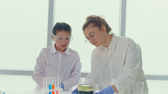 Girl With a Teacher in Lab Coats and Safety Glasses Conducts Experiments