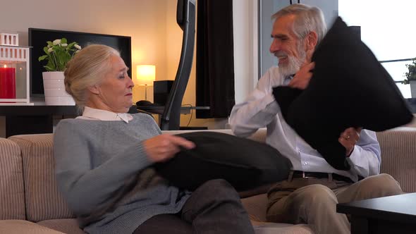 An Elderly Couple Sits on A Couch in An Apartment and Has a Pillow Fight