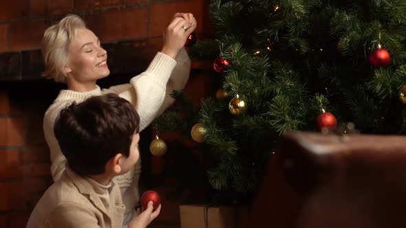 Happy Young Mother and Adorable Child Son Decorating with Colorful Balls of Christmas Tree Flashing