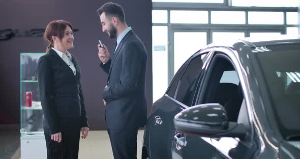 Positive Handsome Male Trader Giving Car Keys To Smiling Successful Female Client