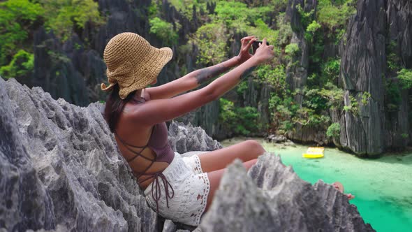 Woman Sitting On Limestone Rocks Taking Photo With Smartphone