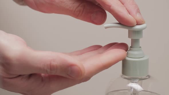 Close up of male hands pushing on a dispenser with liquid transparent soap to wash hands on a white