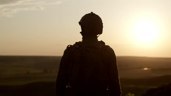 Silhouette of Soldier in Military Uniform with Rifle Against Background of Sunset alt
