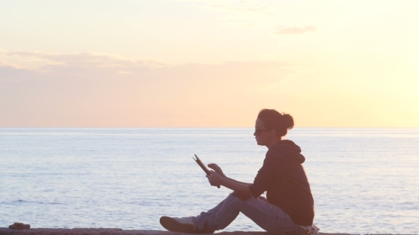 Woman Using a Tablet On The Beach During Sunset