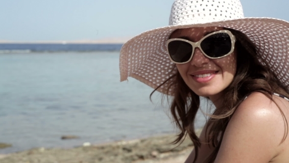 Beautiful Woman In a Hat And Sunglasses Sunbathing On The Beach On a Lounger