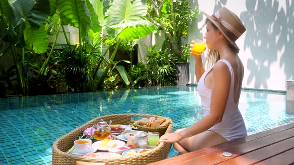 Happy Girl Have Floating Breakfast in Luxury Pool in Hotel Drink Orange Juice