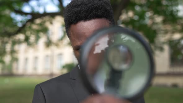 Closeup Portrait of African American Genius Scientist Posing with Magnifying Glass Outdoors
