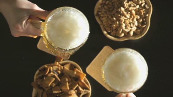 Two Hands With Beer Mugs Clink Over a Black Table alt