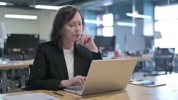 Serious Middle Aged Businesswoman Thinking and Working on Laptop in Office