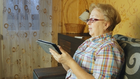 Senior Woman Sitting In Sofa With Electronic Tablet 
