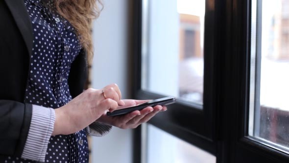 Girl Uses the Phone Standing Near a Window