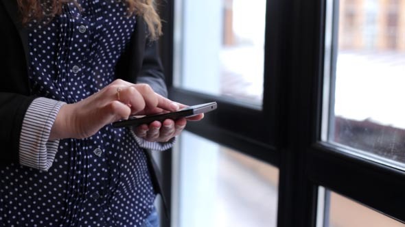 Girl Uses the Phone Standing Near a Window