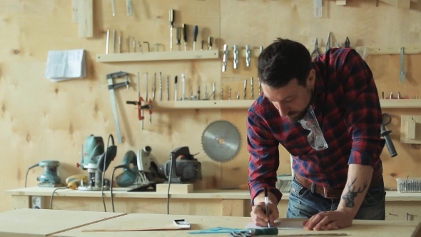 Carpenter Draws The Project In a Carpentry Workshop