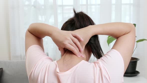 Back view of Asian woman using hands to massage the nape of her neck in physical therapy to reduce p