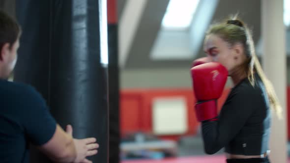 Boxing Training  Young Woman Punching the Bag and Her Coach Standing Behind It