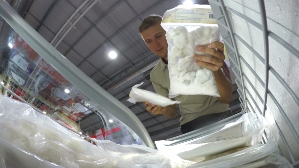 Young Man Choosing Food In Supermarket In Freezer