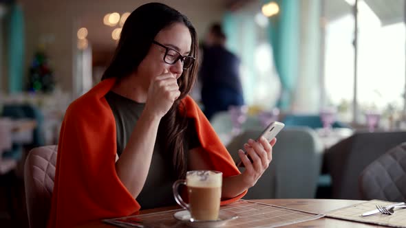 A Business Woman with Glasses Sits in a Cafe During the Day and Talks Via Video Link Via Mobile