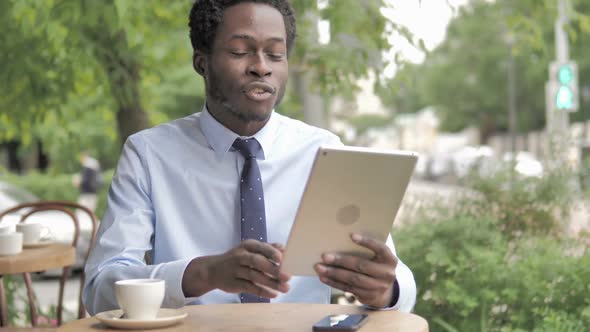 Online Video Chat on Tablet By African Businessman Sitting in Outdoor Cafe