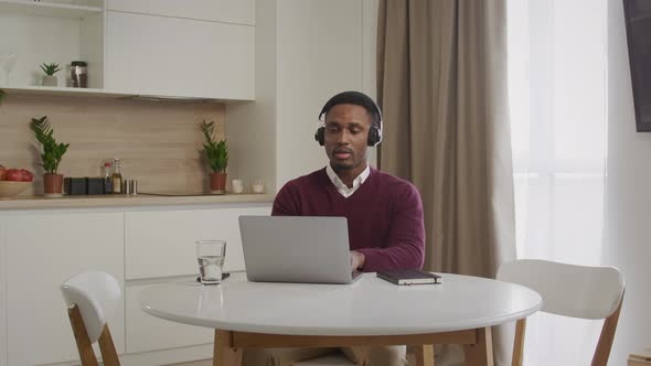 Wide Shot of a Young African American Man in Headphones Working on a Laptop