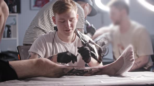 A Session at the Tattoo Salon  Young Man Master Tattooing Big Letters on the Leg