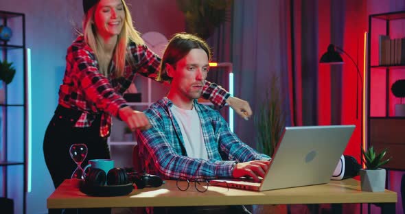 Guy Working on Laptop at Home in the Evening when His Blond Girlfriend Coming to him