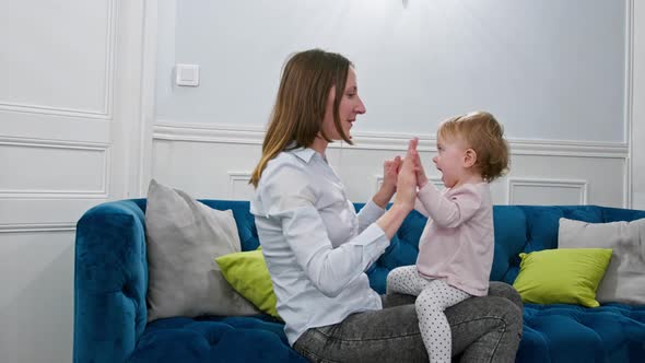 Woman Play with Little Baby Girl Sitting on the Couch at Home